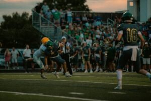 Intense tackle during a high school football game at the stadium with a crowd cheering.